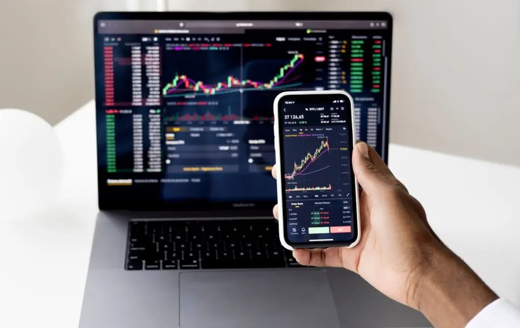 Pessoa acompanhando investimentos no laptop e no smartphone