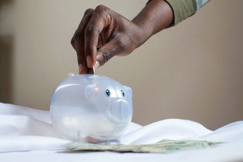MĂŁo colocando moedas em um cofrinho transparente