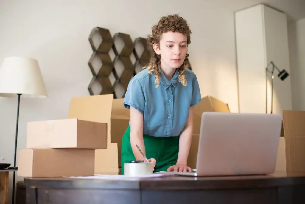 Empreendedora trabalhando no laptop cercada por caixas de pedidos