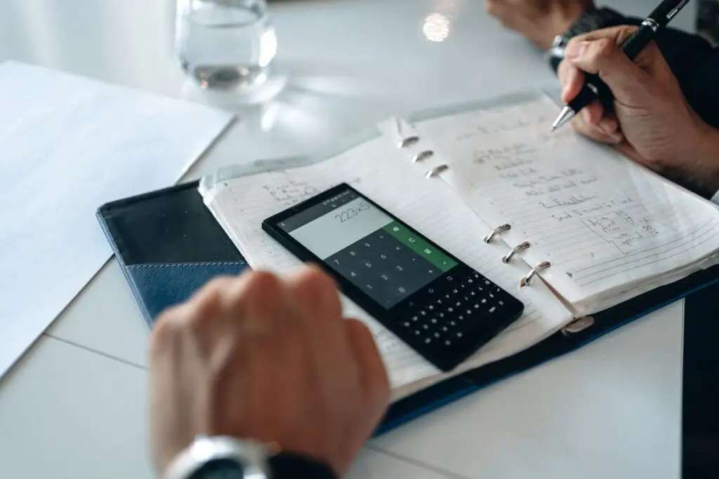 Mãos escrevendo em um caderno com calculadora ao lado