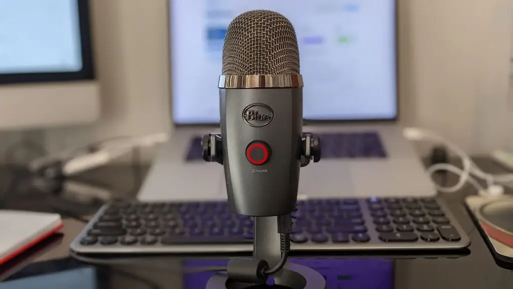 Microfone de podcast em um home office com laptop ao fundo