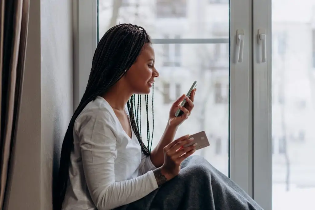 Mulher usando o smartphone com um cartão de crédito na mão