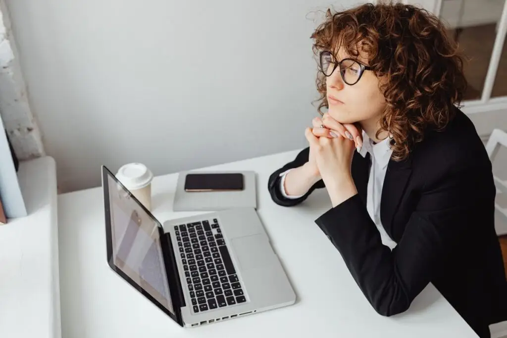 Profissional pensativa sentada diante do laptop no trabalho