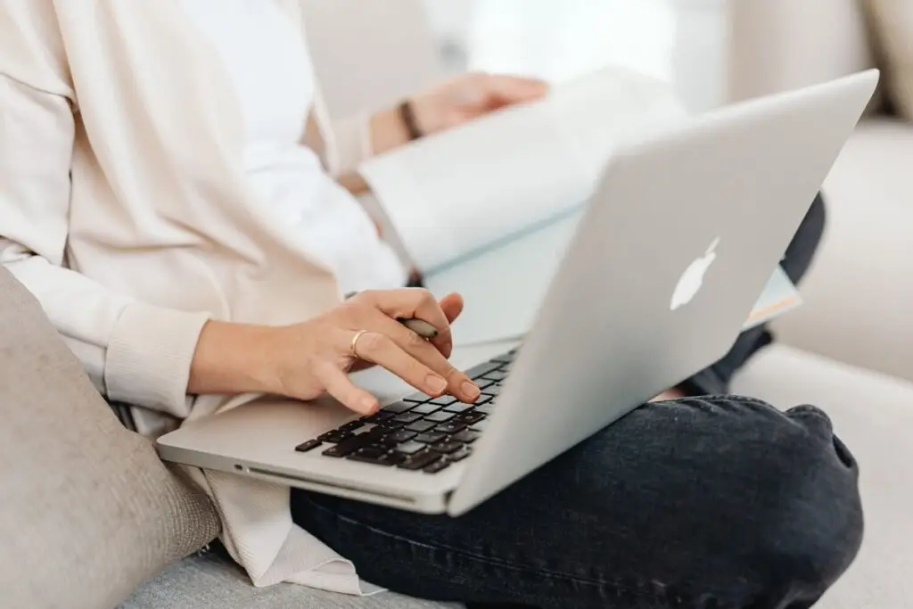 Pessoa digitando no laptop com um livro no colo