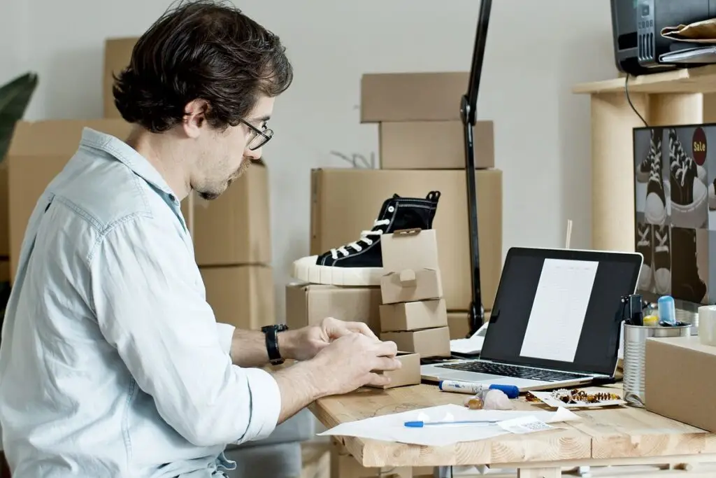 Empreendedor embalando produtos e gerenciando vendas online no laptop